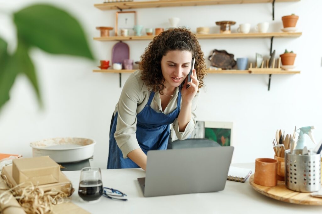 Potter entrepreneur using laptop in workshop, smiling