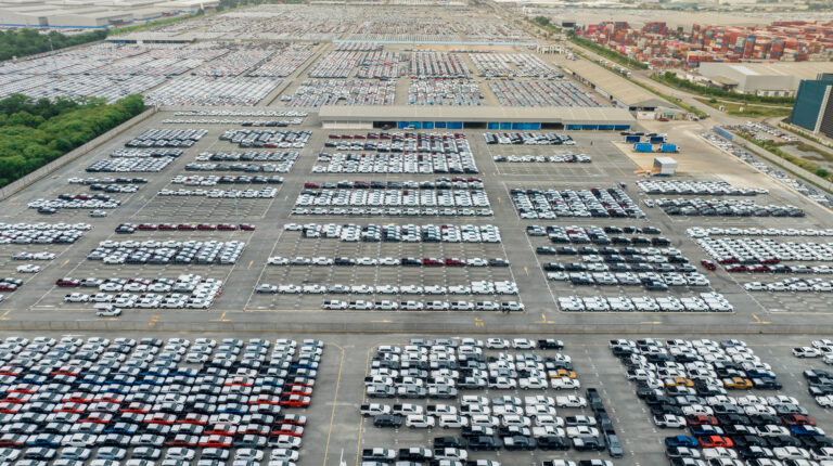 Aerial view of new cars stock at factory parking lot. Above view many cars parked in a row. Auto